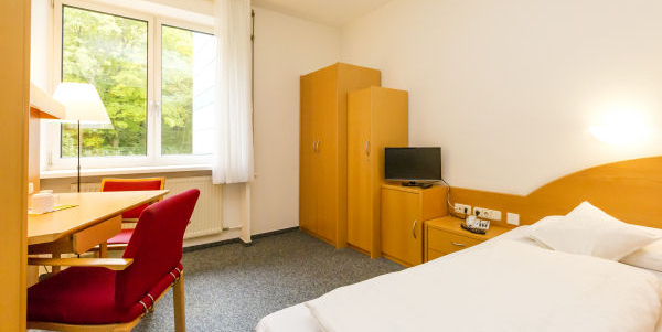 Zimmer mit Bett, Schränke, Tisch und Stühle vor dem Fenster Zimmer mit Bett, Schränke, Tisch und Stühle vor dem Fenster