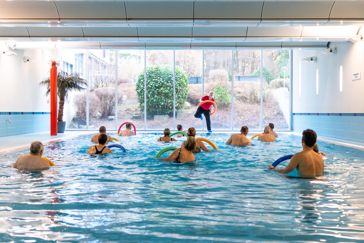 Rehabilitandengruppe mit Schwimmnudel bei der Aquagymnastik im Schwimmbad mit Therapeutin 